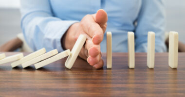 A man's hand preventing a set of a dominos from falling.