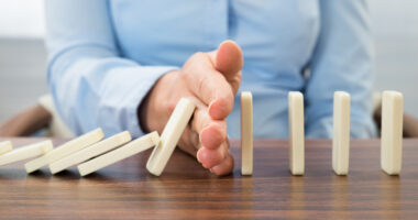 A man's hand preventing a set of a dominos from falling.