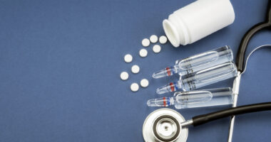 pills in a bottle, a set of shots, and a stethoscope on a blue background