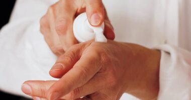 person in white doctor coat applying lotion to hands