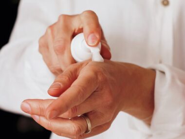 person in white doctor coat applying lotion to hands