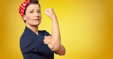 A woman posing like Rosie the Riveter flexing her arm on a yellow background