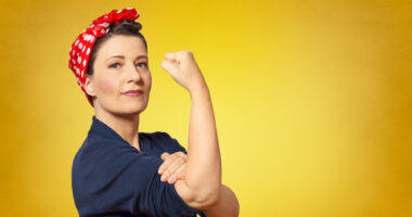 A woman posing like Rosie the Riveter flexing her arm on a yellow background