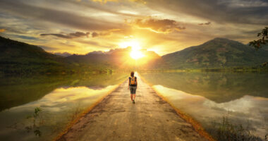 A solo traveler walking on a road at sunset with mountains in the background