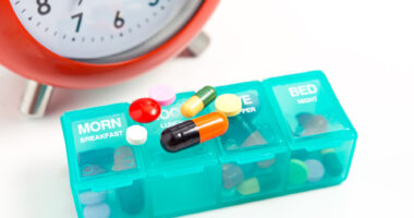 clock with pill organizer and medications on top of it