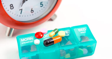 clock with pill organizer and medications on top of it