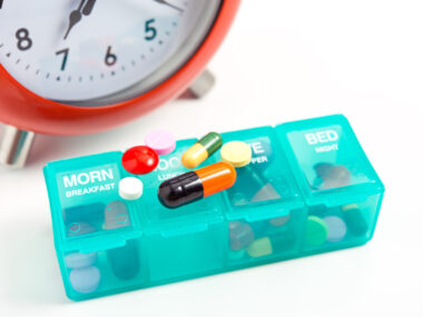 clock with pill organizer and medications on top of it