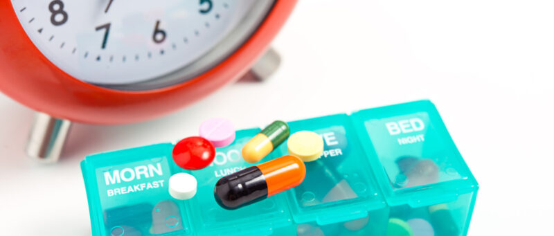clock with pill organizer and medication on top of it 