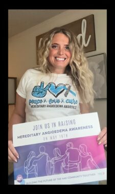 A woman stands holding a sign saying "Join us in raising hereditary angiodema awareness." 