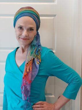 A woman with her head wrapped in a scarf stands with her left hand on her hip.